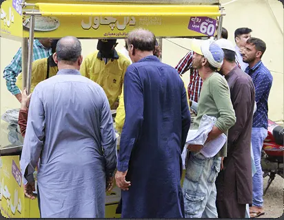 Customers standing at a yellow Rizq Khana food cart, seen from behind, with a Rs 60 sign visible